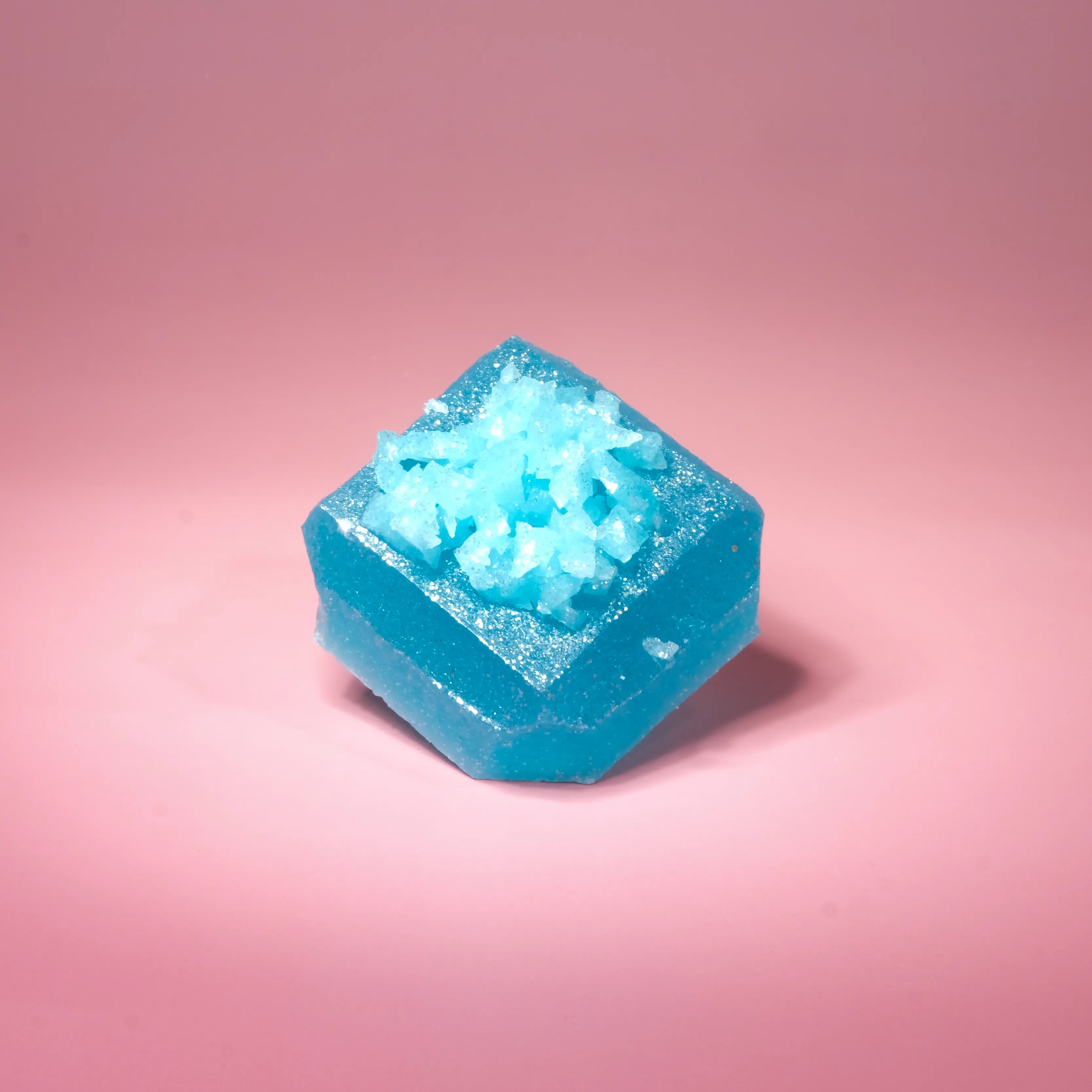 Single Blue Raspberry Lapis Silky Gem crystal candy with a faceted blue jelly exterior and icy sugar crystal center on a pink backdrop.