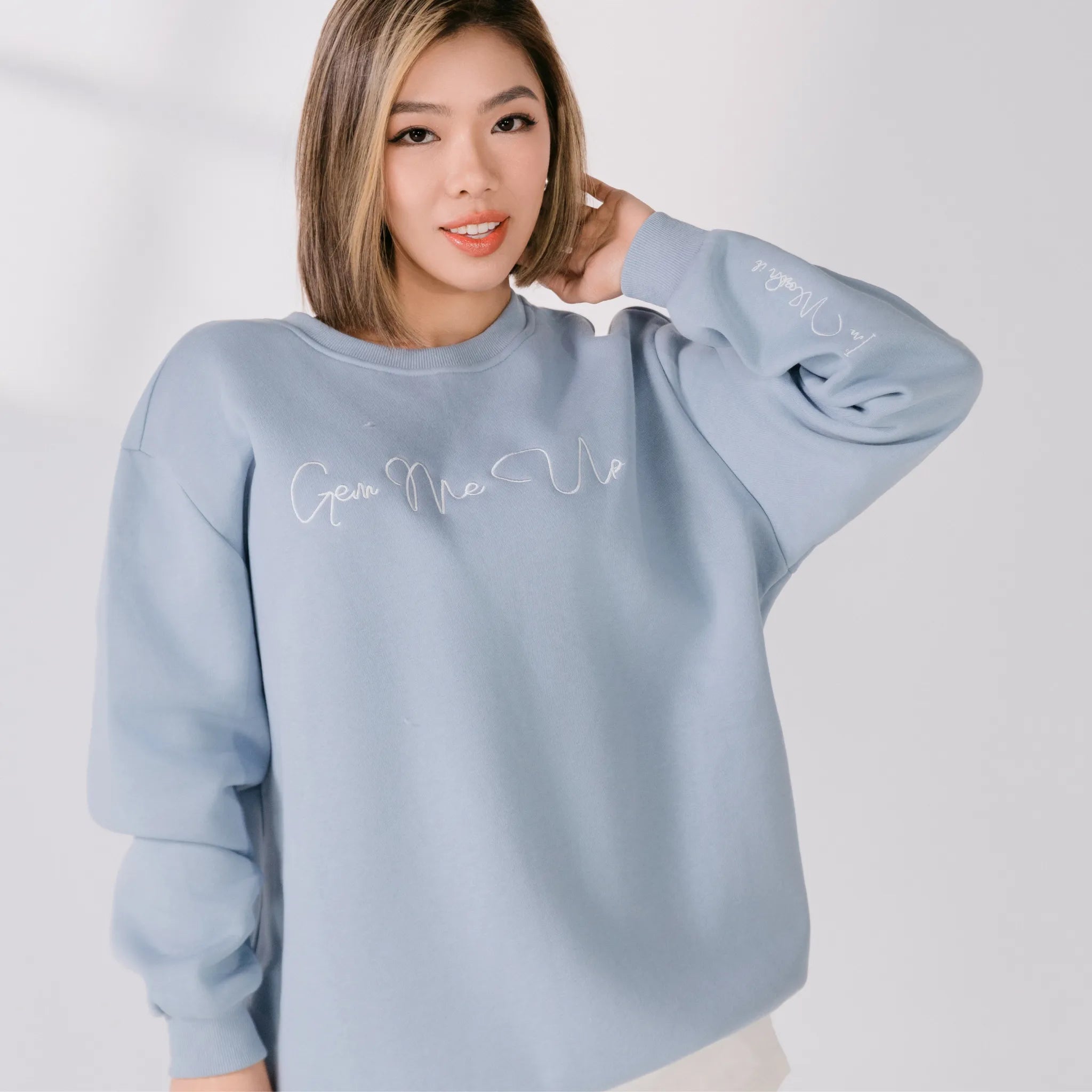 Woman wearing a light blue sweatshirt with text on a plain background
