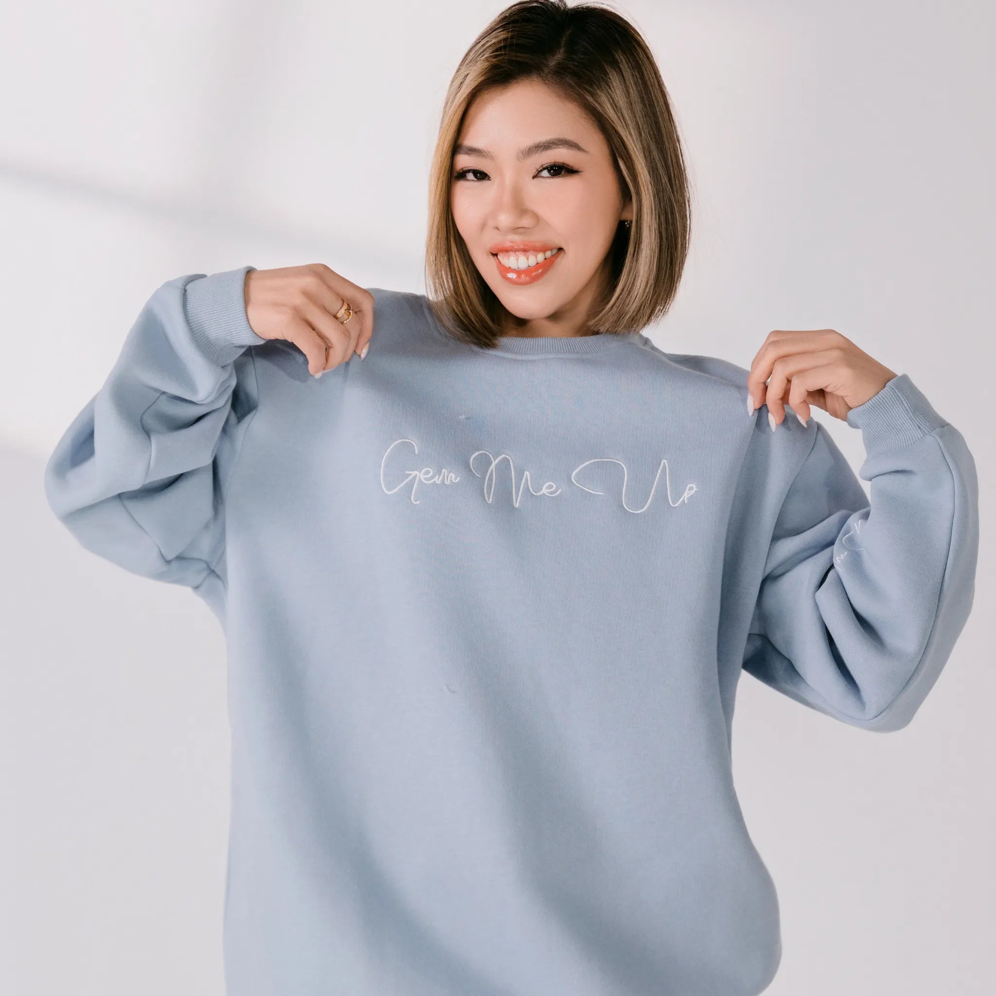 Woman wearing a light blue sweatshirt with text on it against a plain background