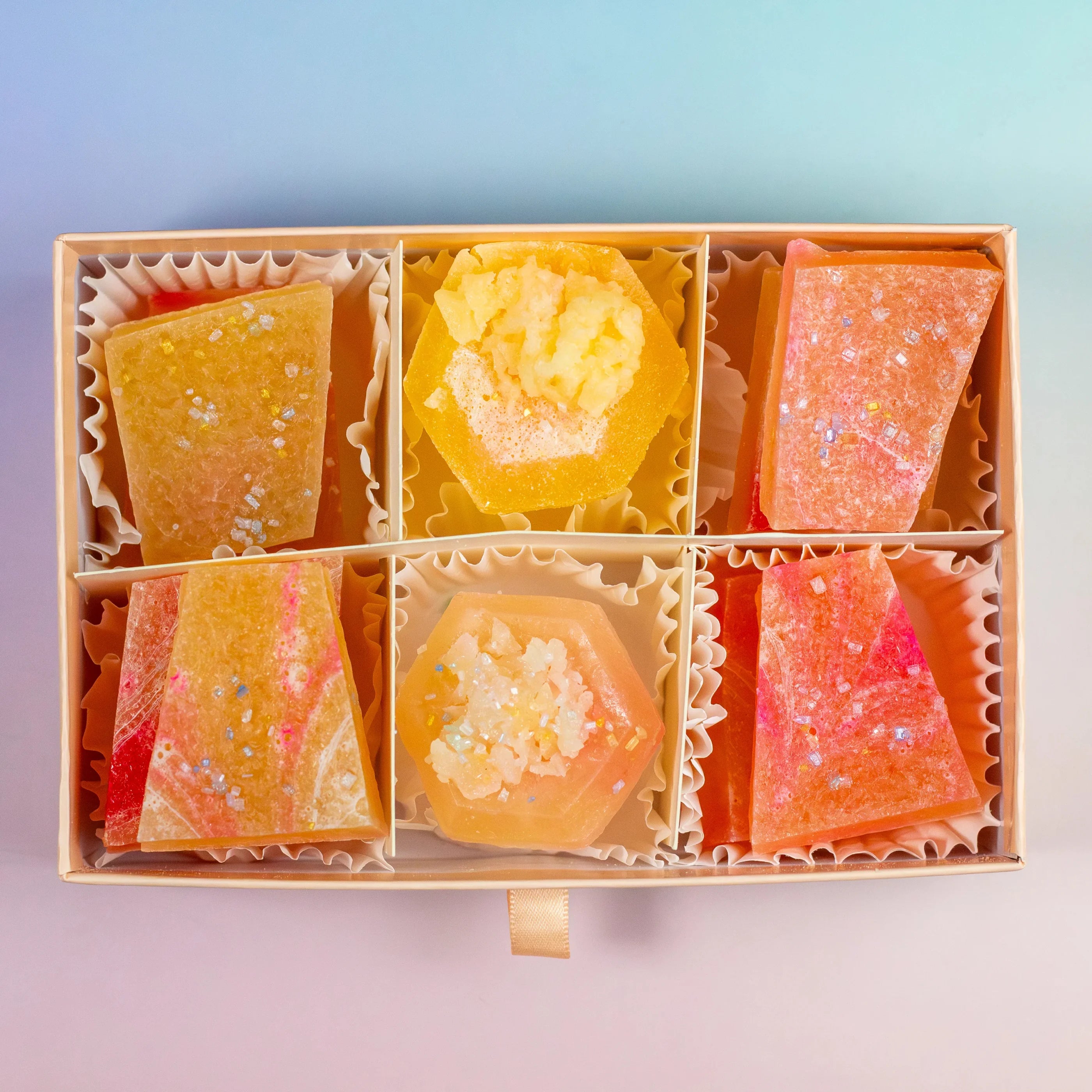 A box of assorted Silky Gem® Peach Moonstone candies with a mix of orange and peach colors and sparkling inclusions, presented in a partitioned cardboard box.