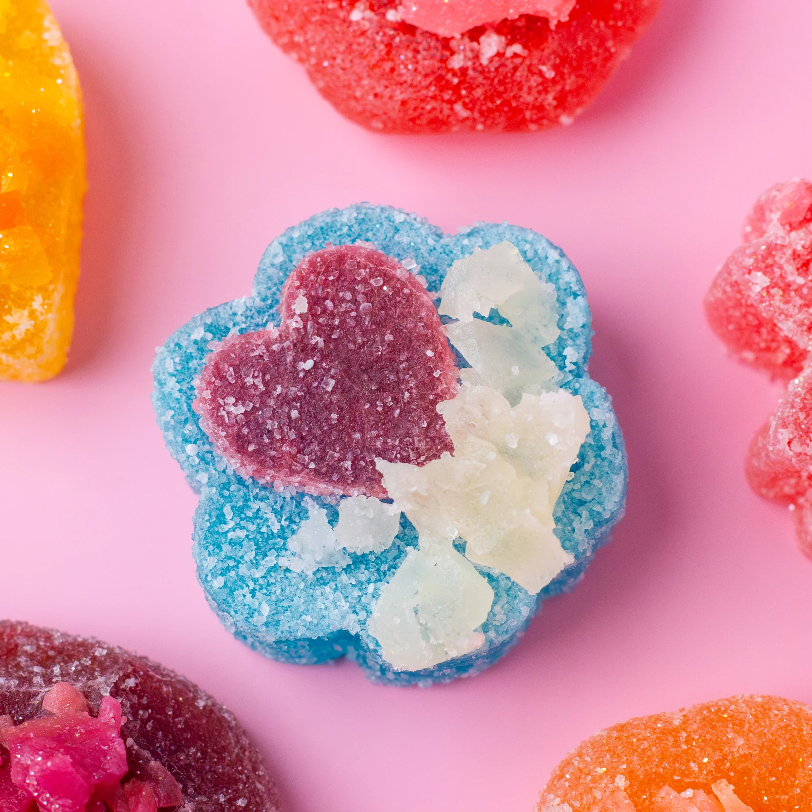 Colorful gummy candy with heart and leaf design on a pink background