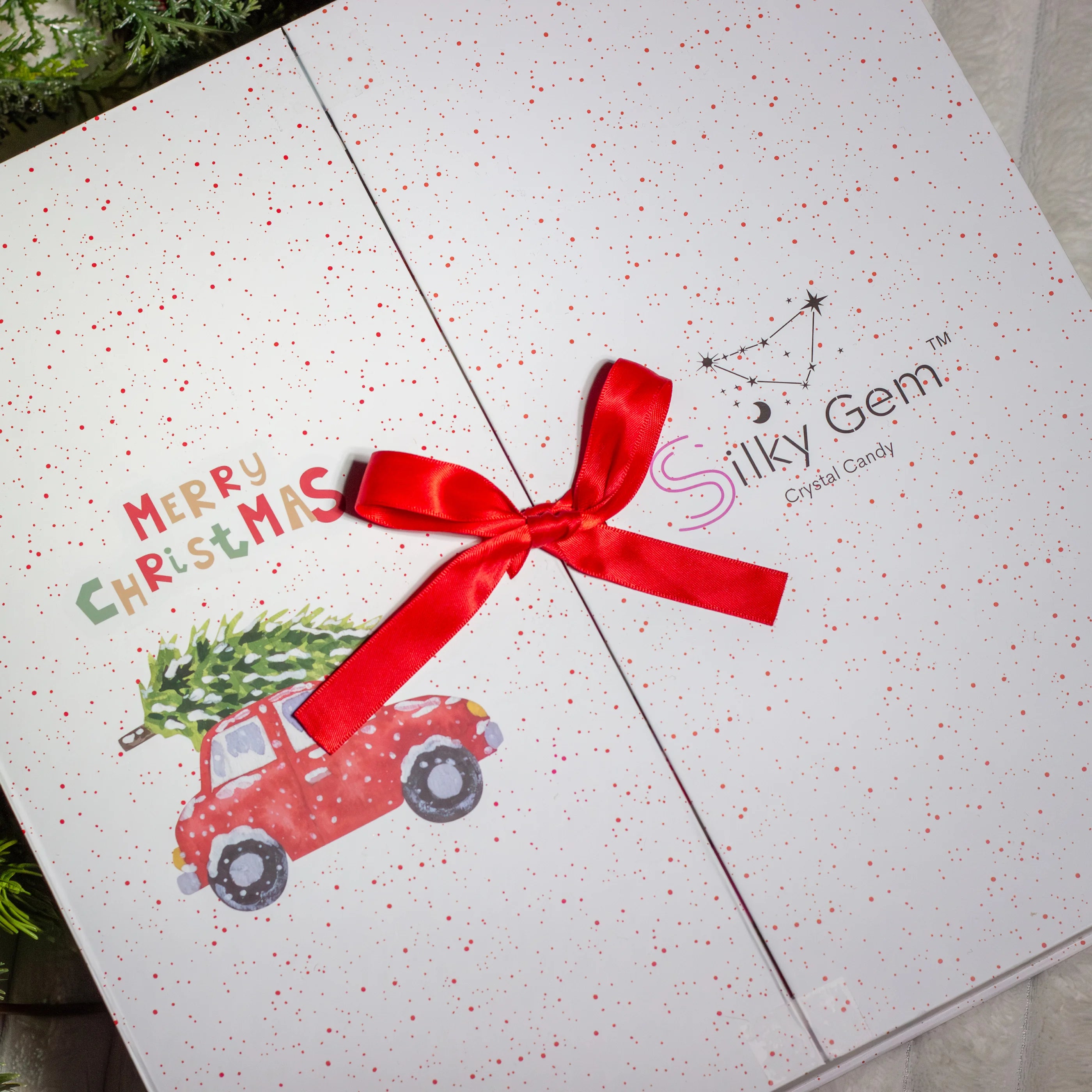 Gift box with a red ribbon, Christmas tree, and truck design on a white background with 'Silky Gem' branding.