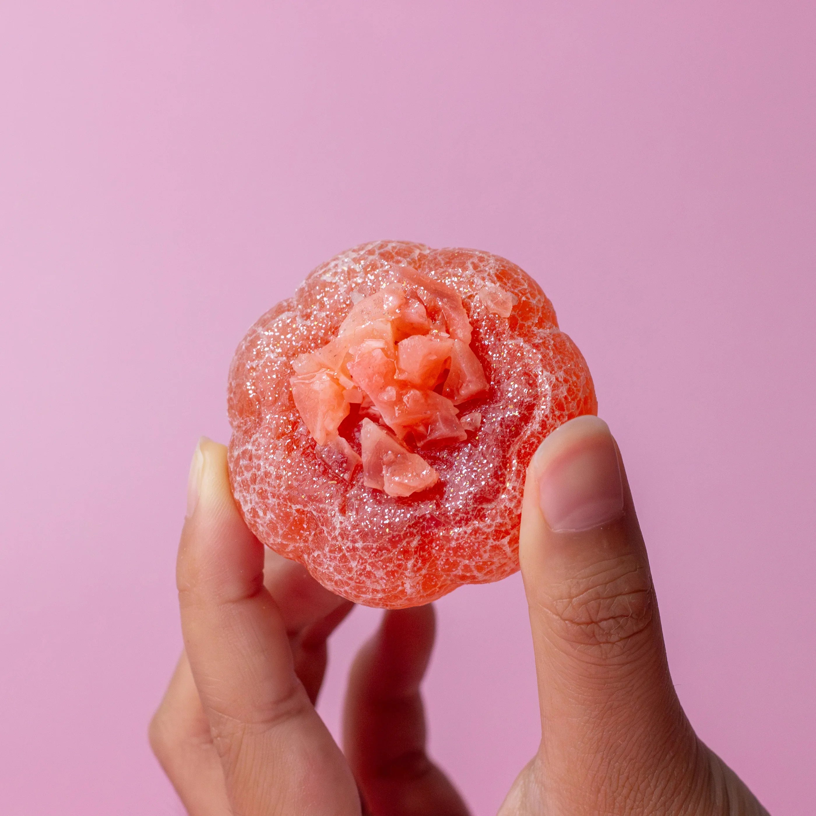 Hand holding a pink gummy candy against a pink background