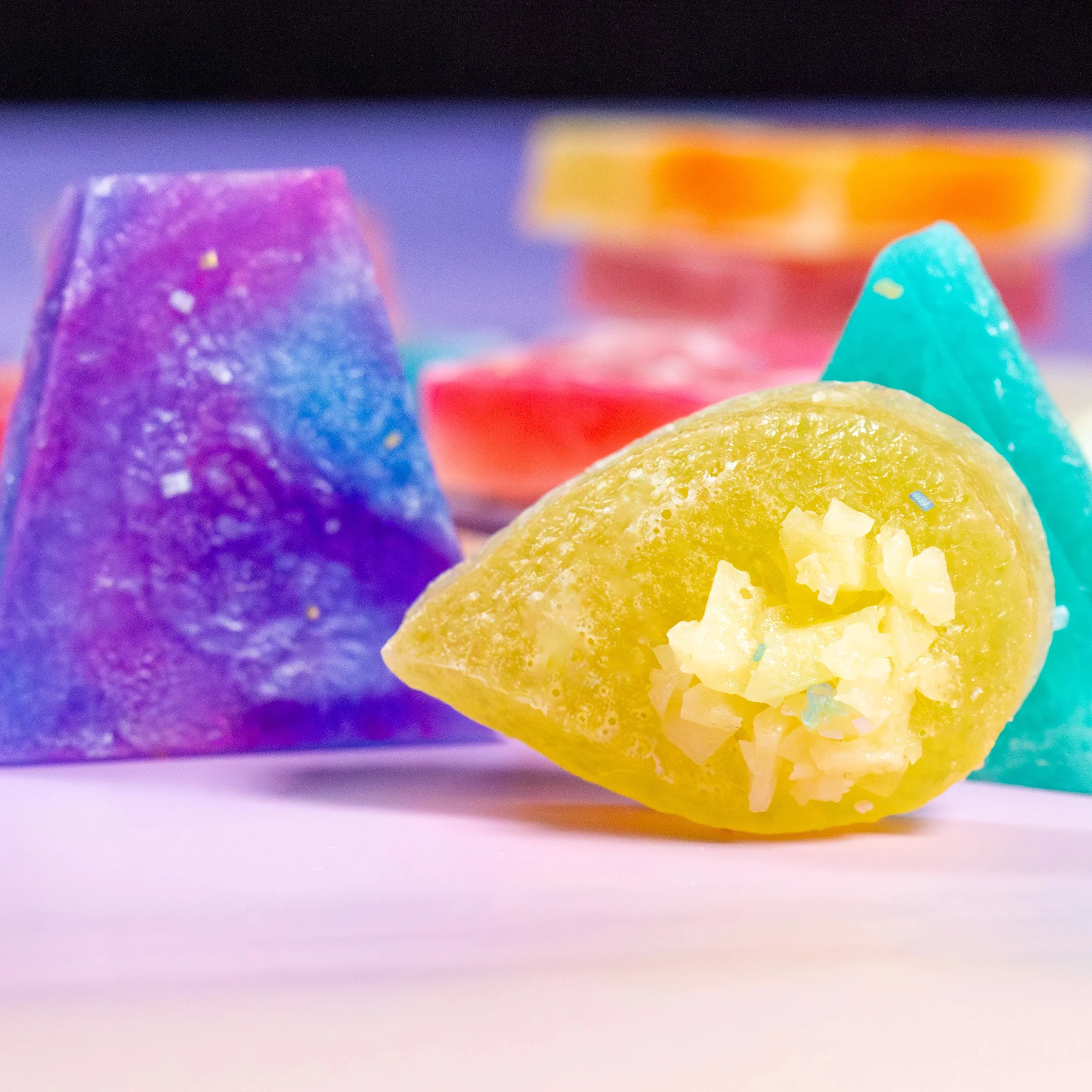 Colorful gummy candies with a purple, green, and orange candy in the background.