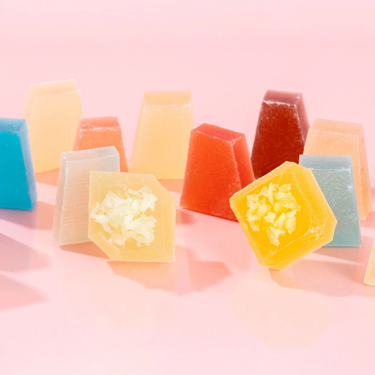 A collection of colorful, crystal-cut candy pieces in various shapes, including pyramids and cubes, arranged on a pink background.