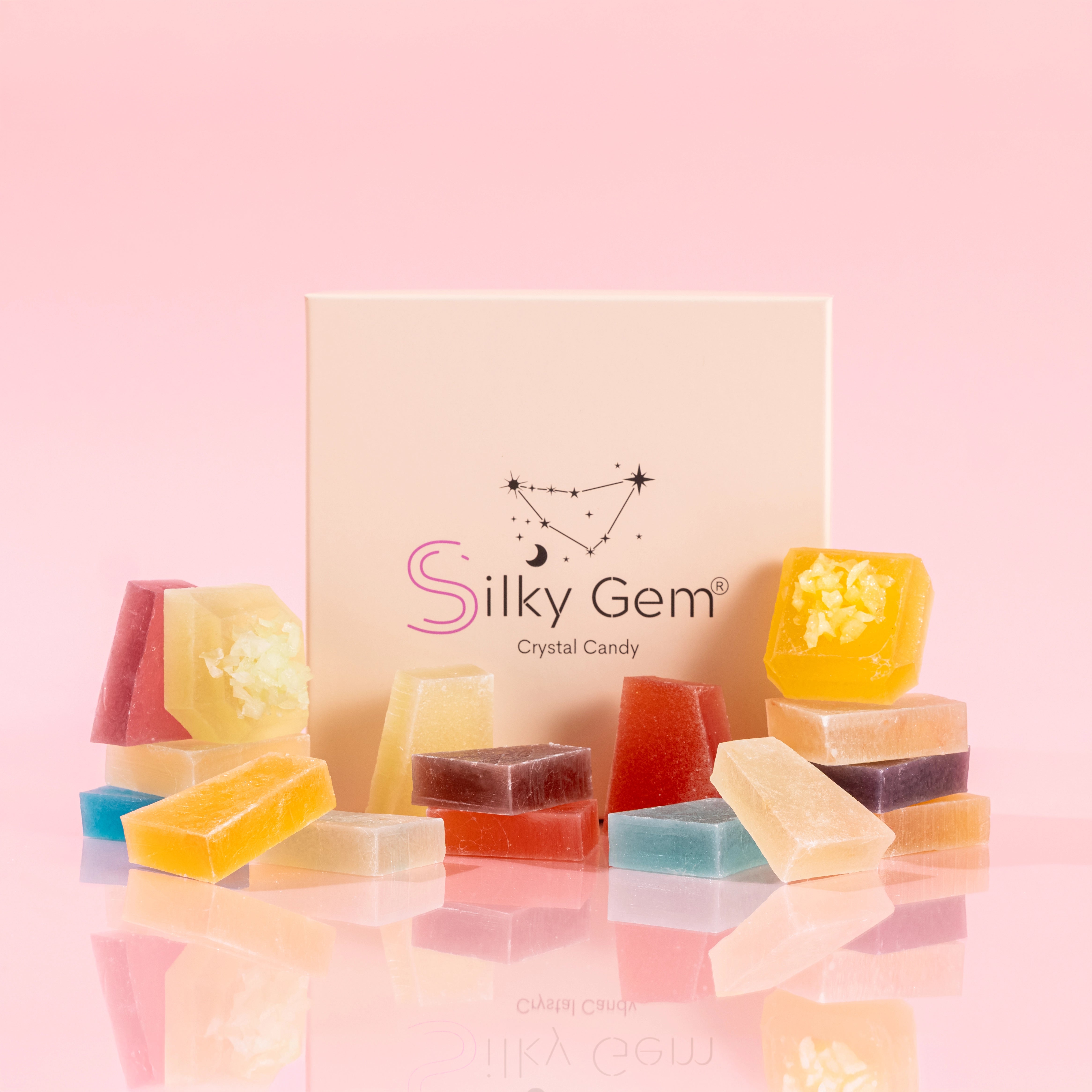 Silky Gem® Treasure Box gift box displayed with an assortment of vibrant, crystal-cut candy pieces stacked in front on a pink background.