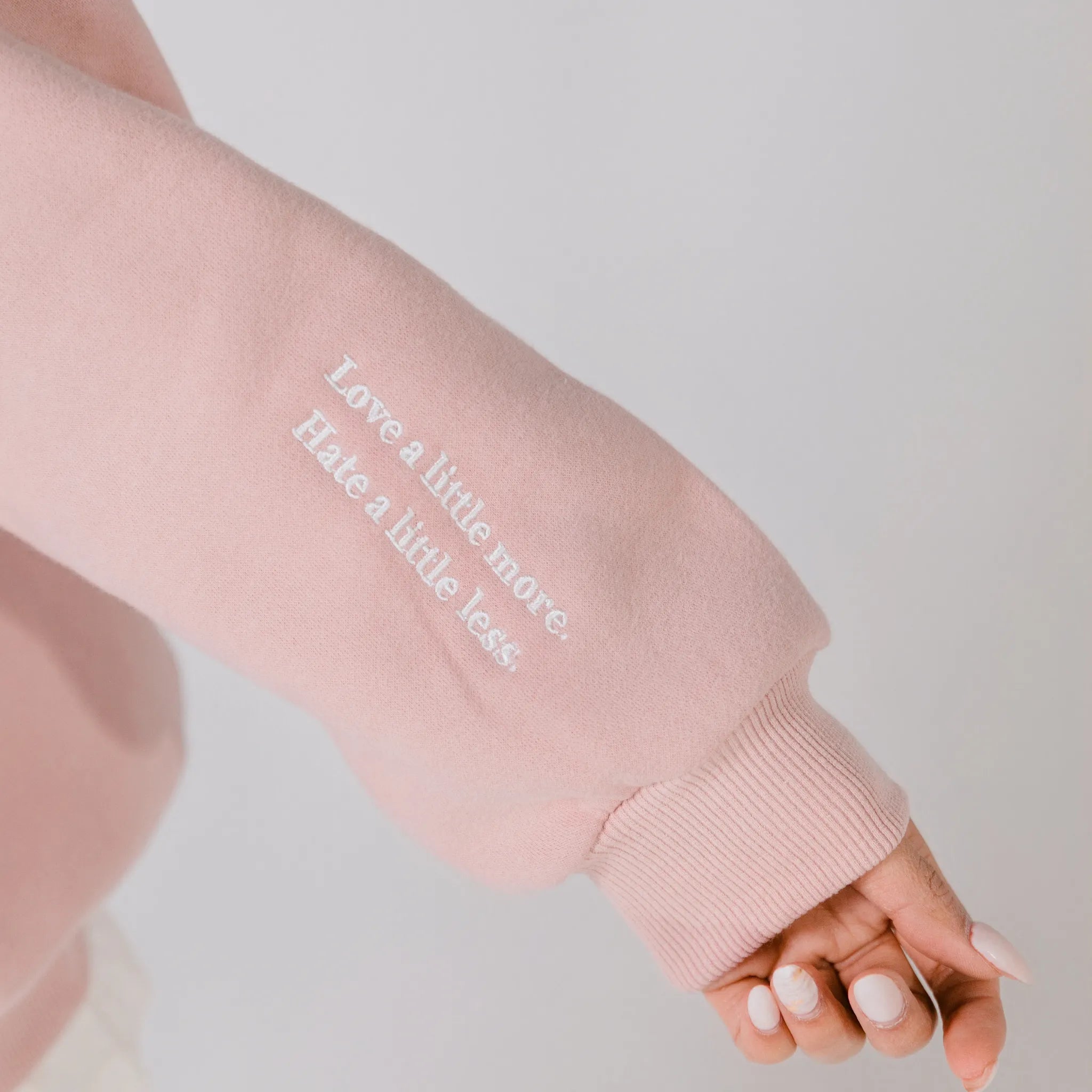 Pink sweatshirt sleeve with embroidered text on a plain background