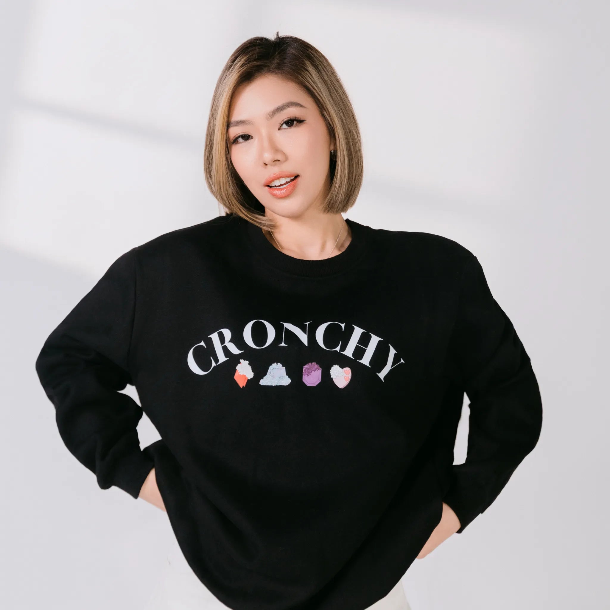 Person wearing a black sweatshirt with 'CRONCHY' and colorful icons on a white background