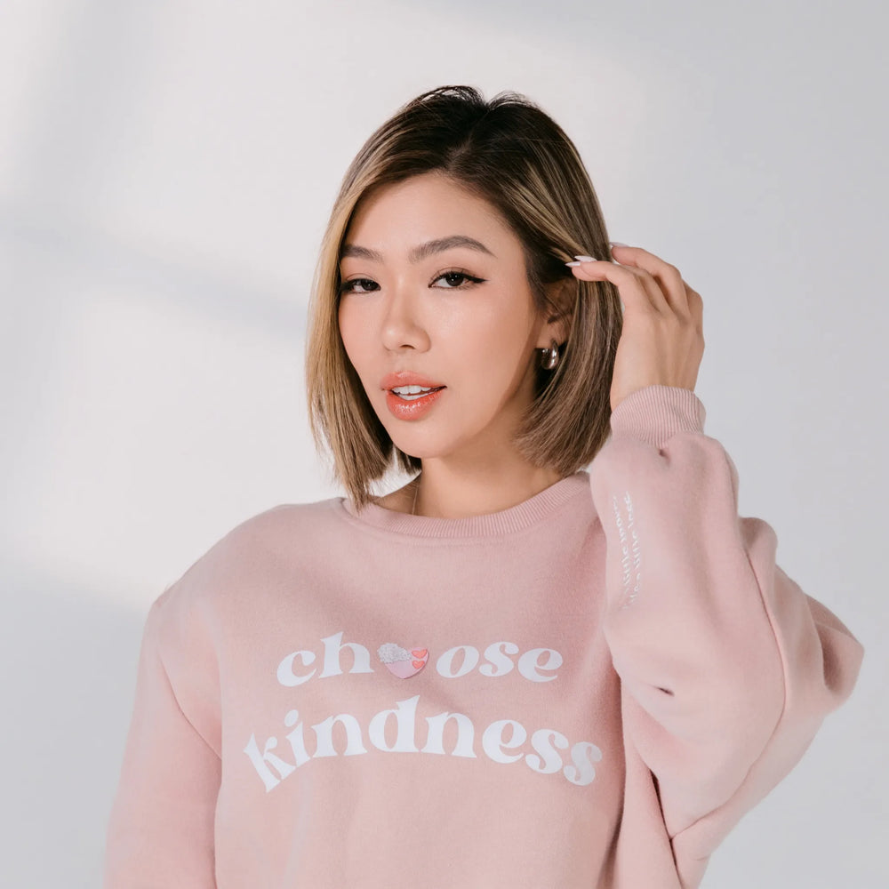 Woman wearing a pink sweatshirt with 'choose kindness' text on a white background