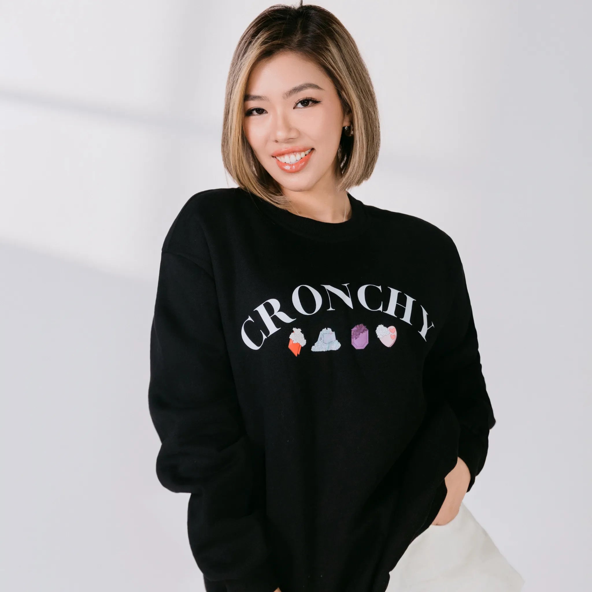 Person wearing a black sweatshirt with 'CRONCHY' and colorful icons on a white background