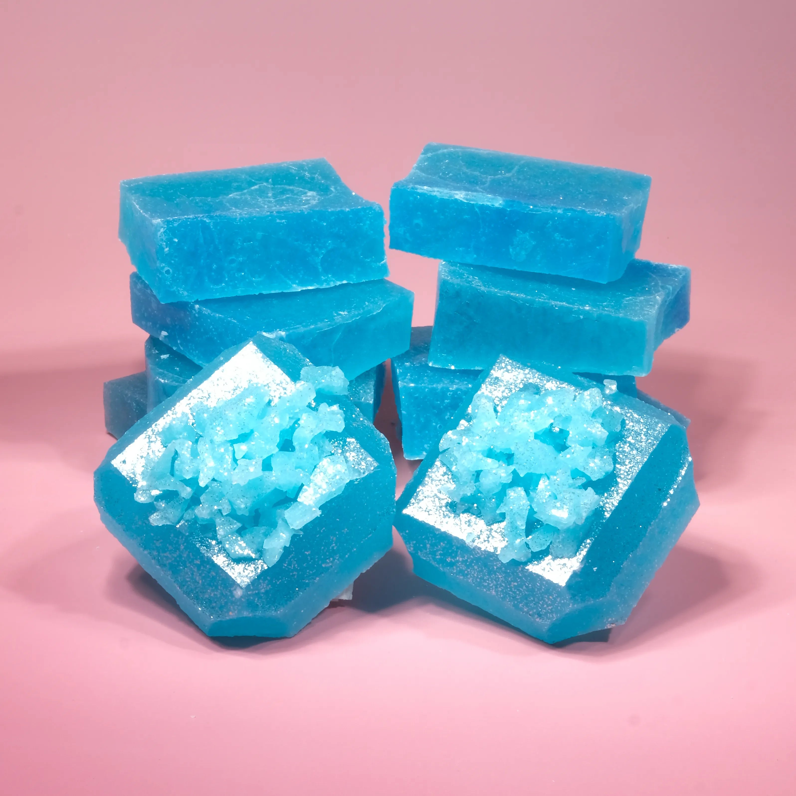 Stacked Blue Raspberry Lapis Silky Gem crystal candies with translucent blue jelly centers and sparkling sugar-coated tops on a pink background.