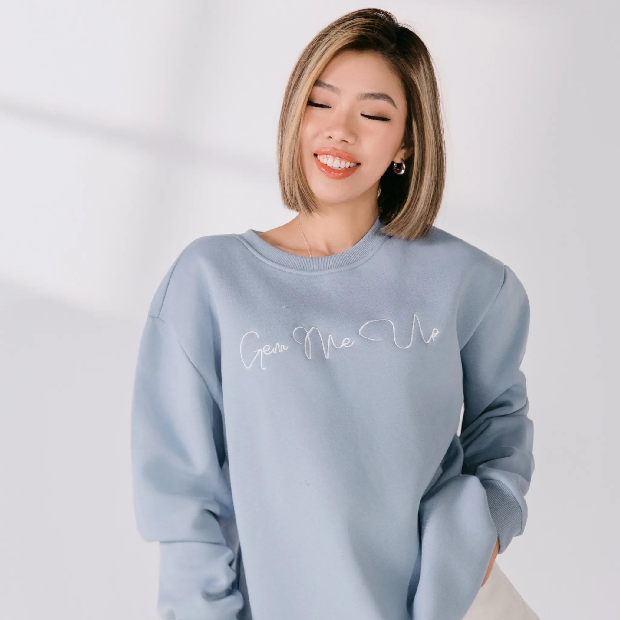 Woman wearing a light blue sweatshirt with text on a plain background