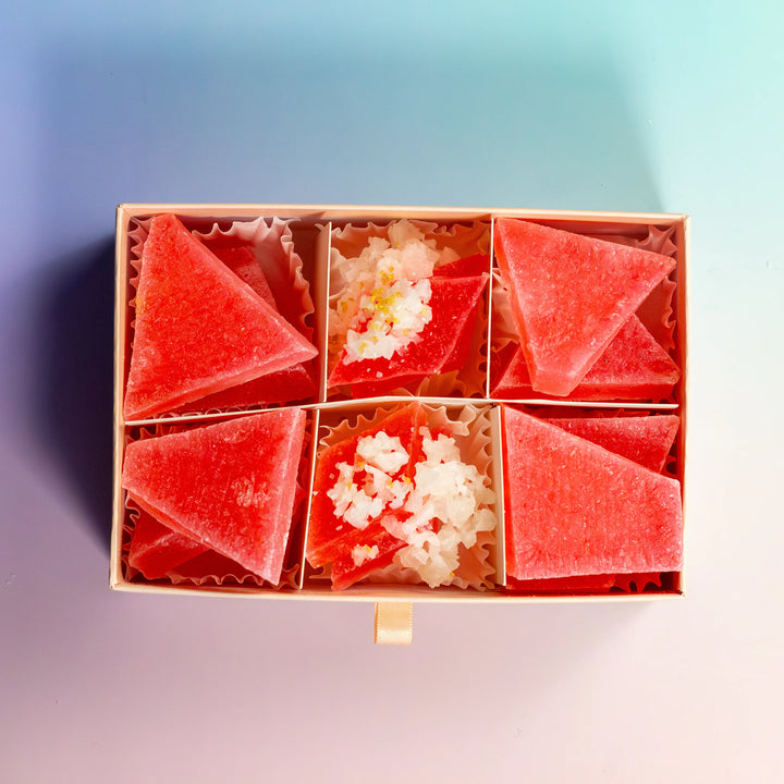 A box of red, triangular-shaped Strawberry Rubellite crystal candies with a creamy white center displayed in a compartmentalized box.
