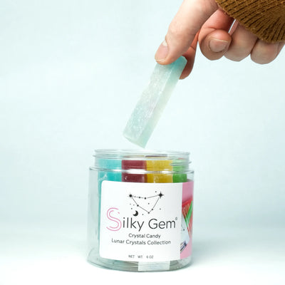 Hand lifting a translucent crystal candy from a Silky Gem Lunar Crystals jar, revealing colorful crystal candies inside, symbolizing Lunar New Year celebration.