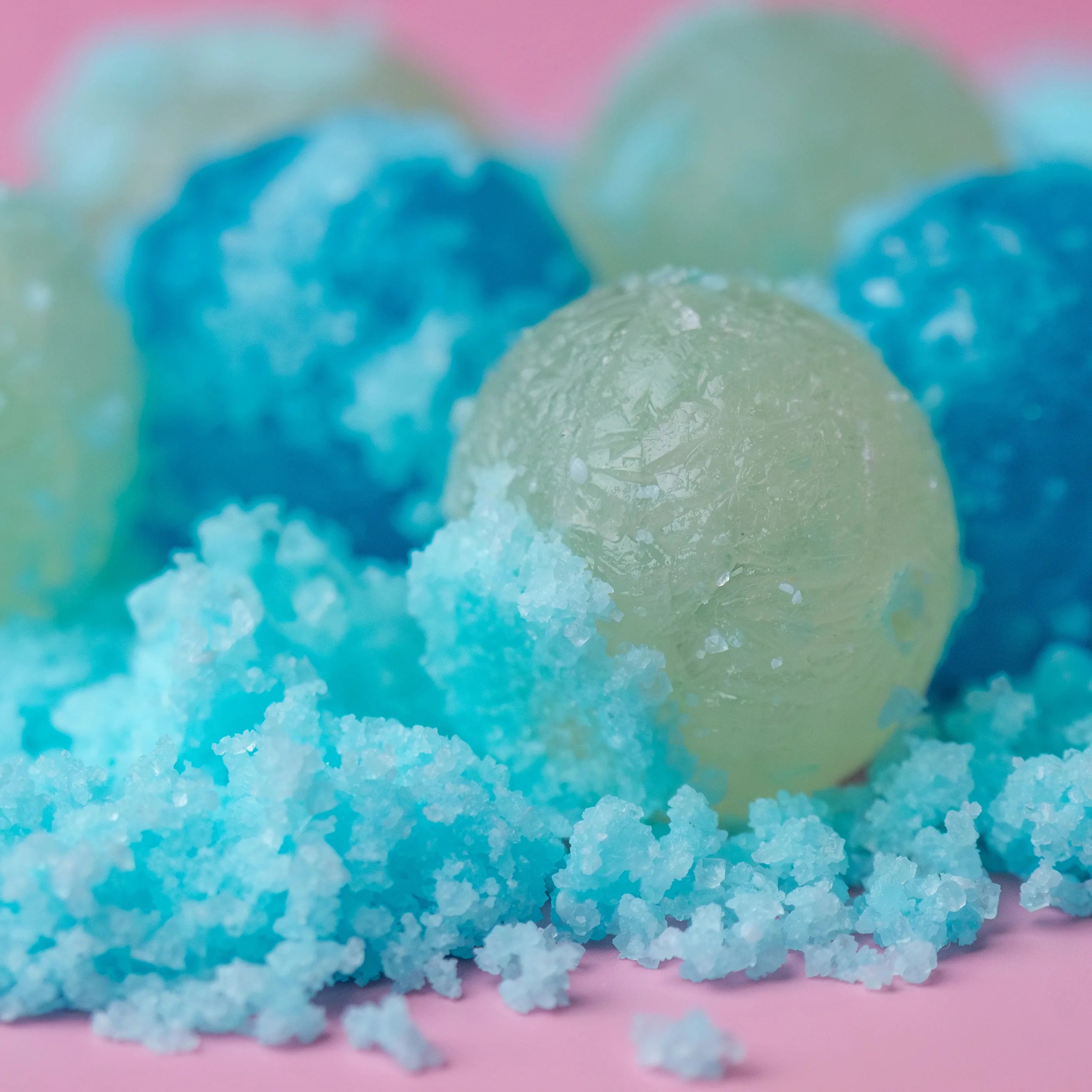 Close-up of green and blue bath bombs with a pink background