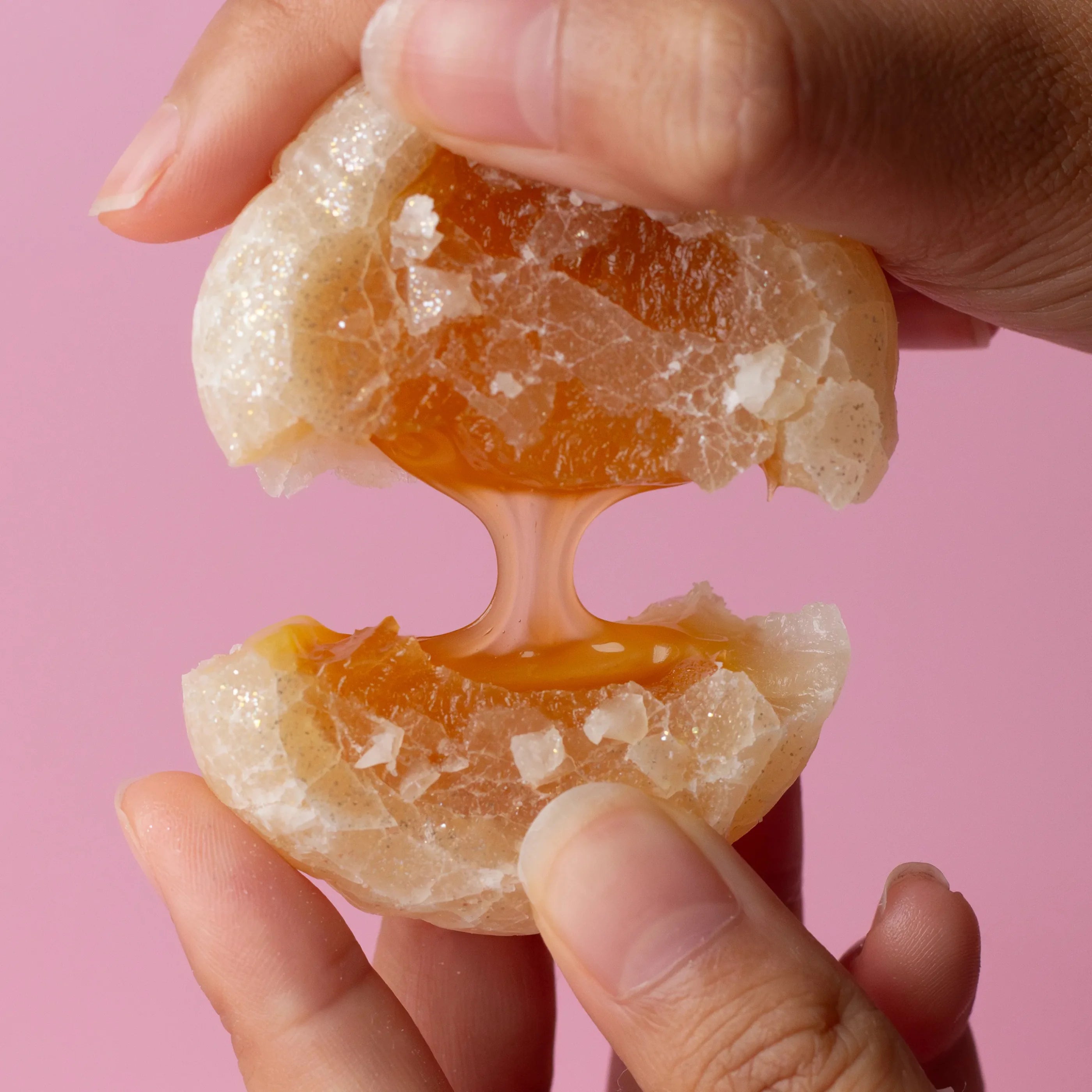 Hand holding a peeled orange against a pink background