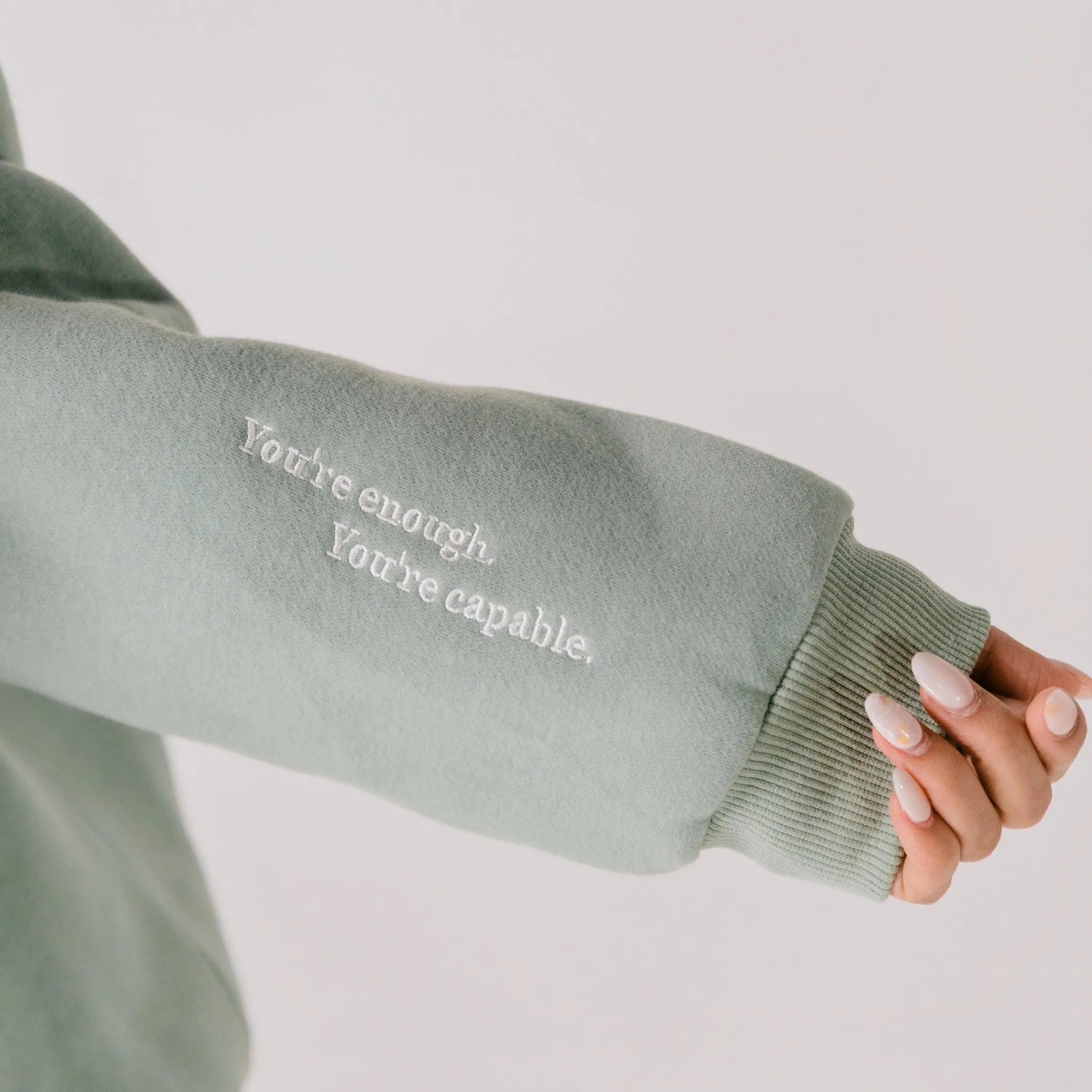Sage green sweatshirt sleeve with motivational text on a plain background