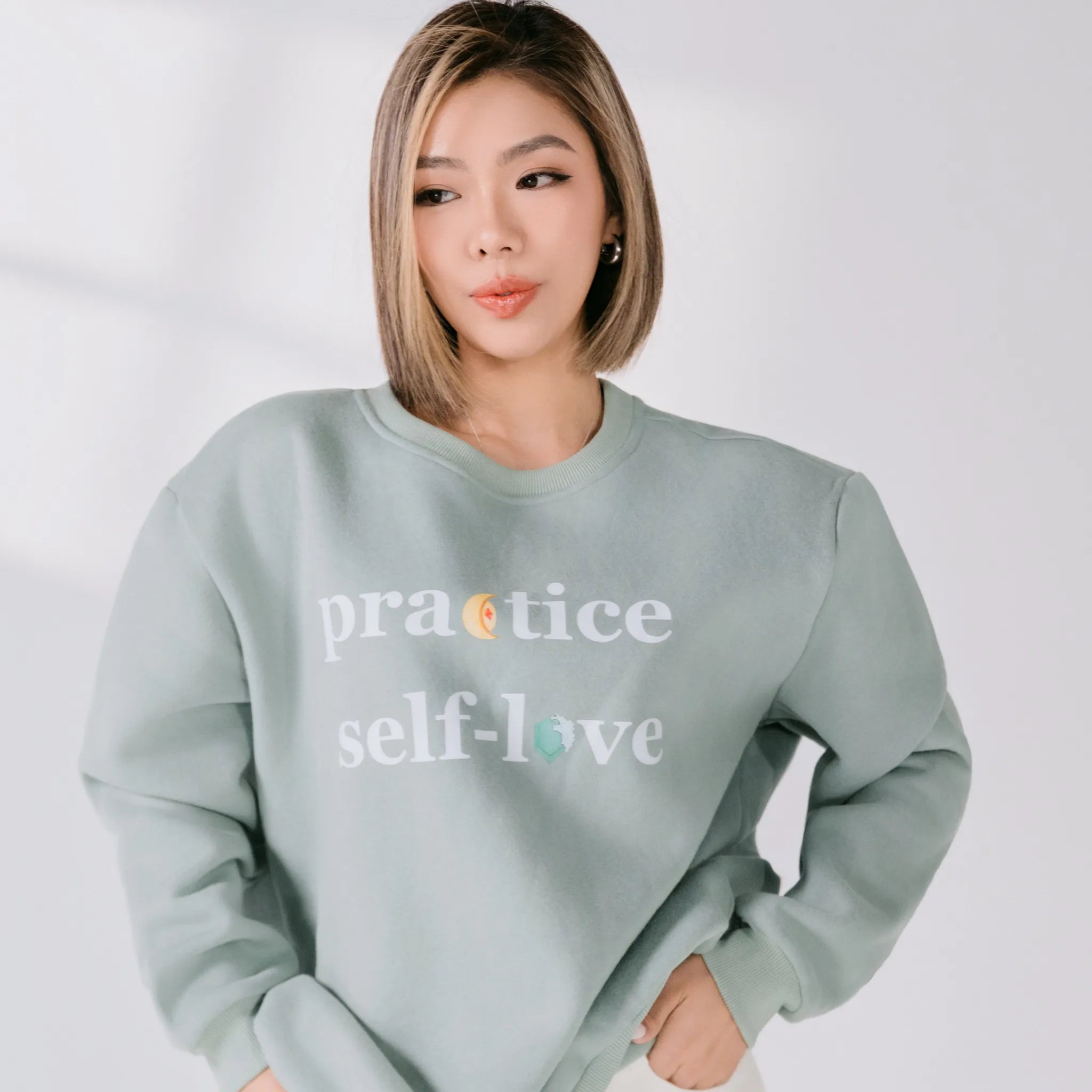 Person wearing a light blue sweatshirt with 'practice self-love' text on a plain background