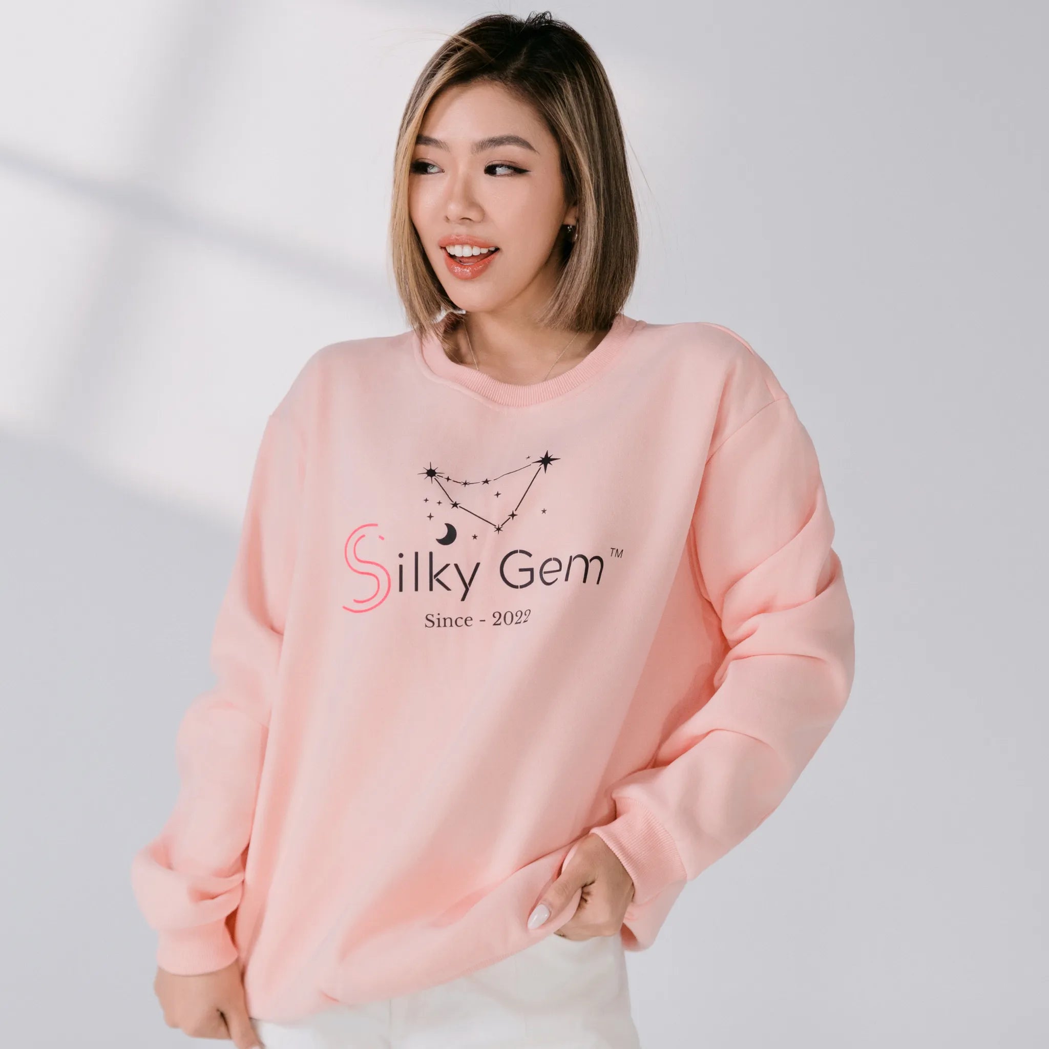 Person wearing a pink sweatshirt with 'Silky Gem' logo on a light gray background