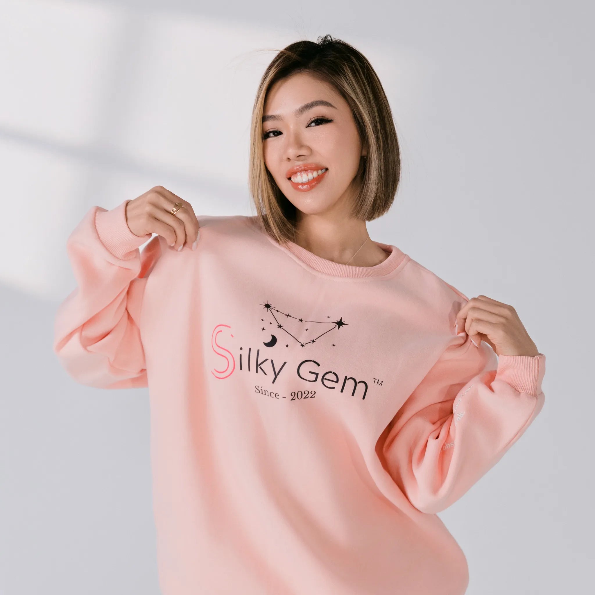 Woman wearing a pink sweatshirt with 'Silky Gem' branding on a plain background