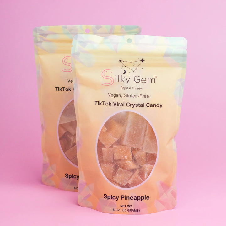 Two packages of Silky Gem Spicy Pineapple crystal candy on a pink background