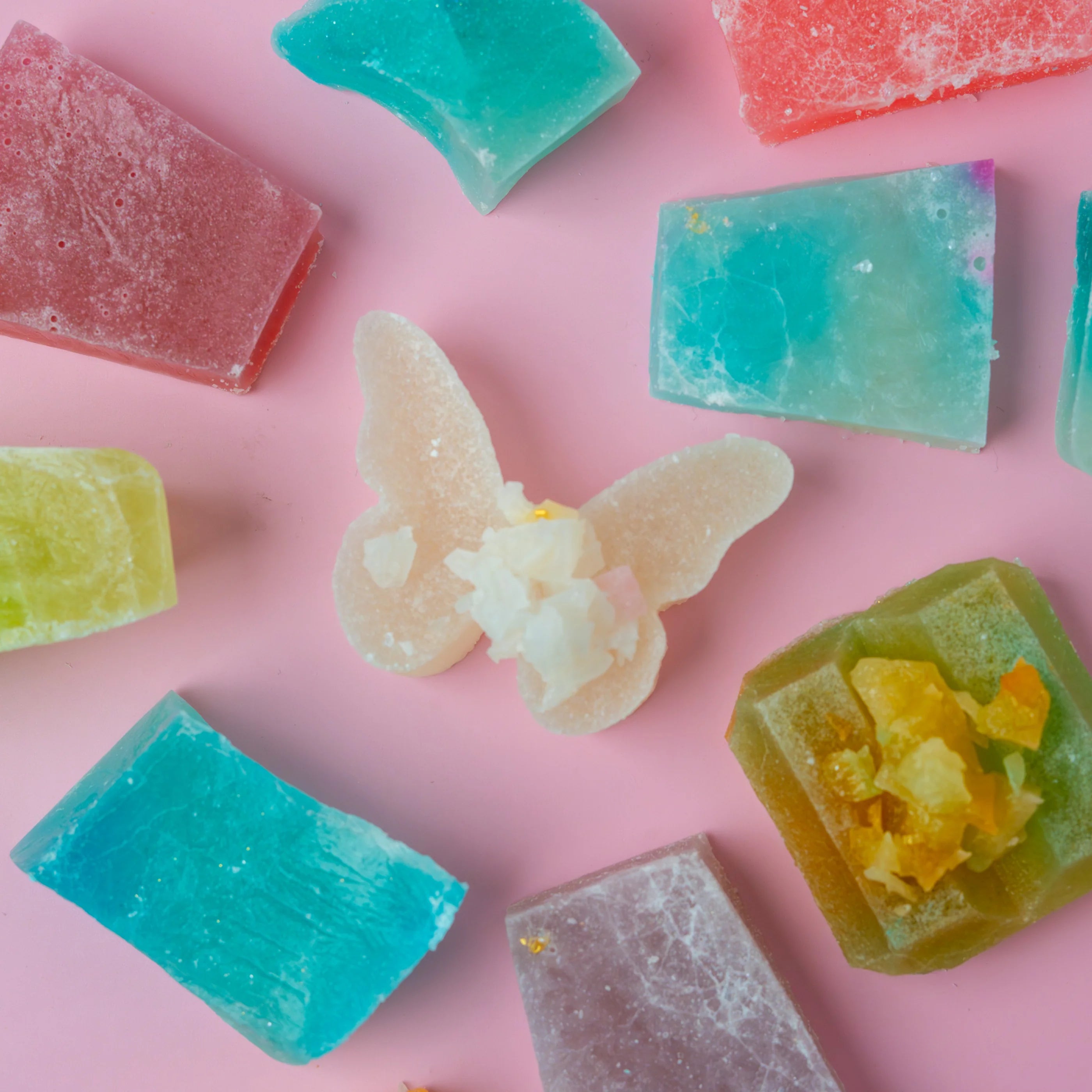 Colorful butterfly-shaped and block-shaped soap bars on a pink background