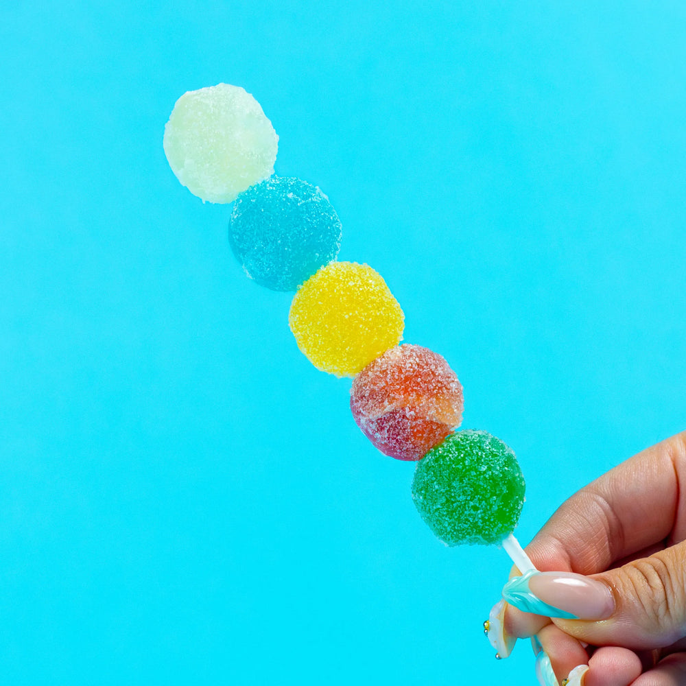 Hand holding a Sizzle Pop skewer with five colorful sour crystal candies
